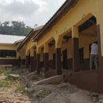 A single-storey school building with a person working outside, hills behind