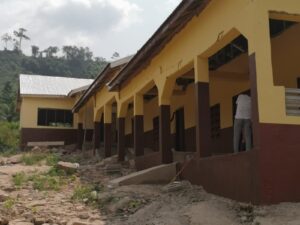 A single-storey school building with a person working outside, hills behind