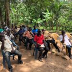 A group of people seated outdoors in the shade of trees