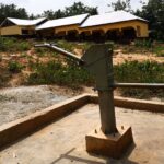 A hand water pump in the foreground with a school building behind