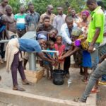 A crowd gathered around a hand water pump